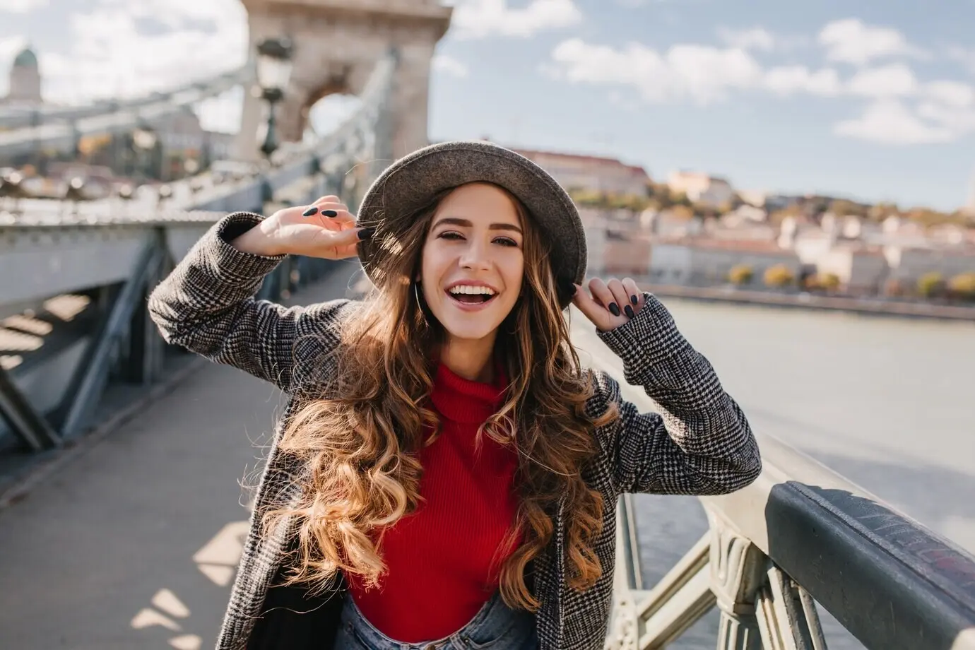 Beautiful smiling woman with long curly hair happily posing on a bridge against a blurred background.